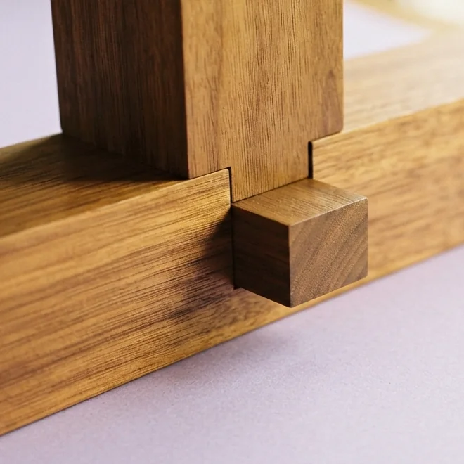 A
  close-up of a timber joint in walnut, where an upright post meets a horizontal
  rail and the end of the tenon passes through and stands proud of it.